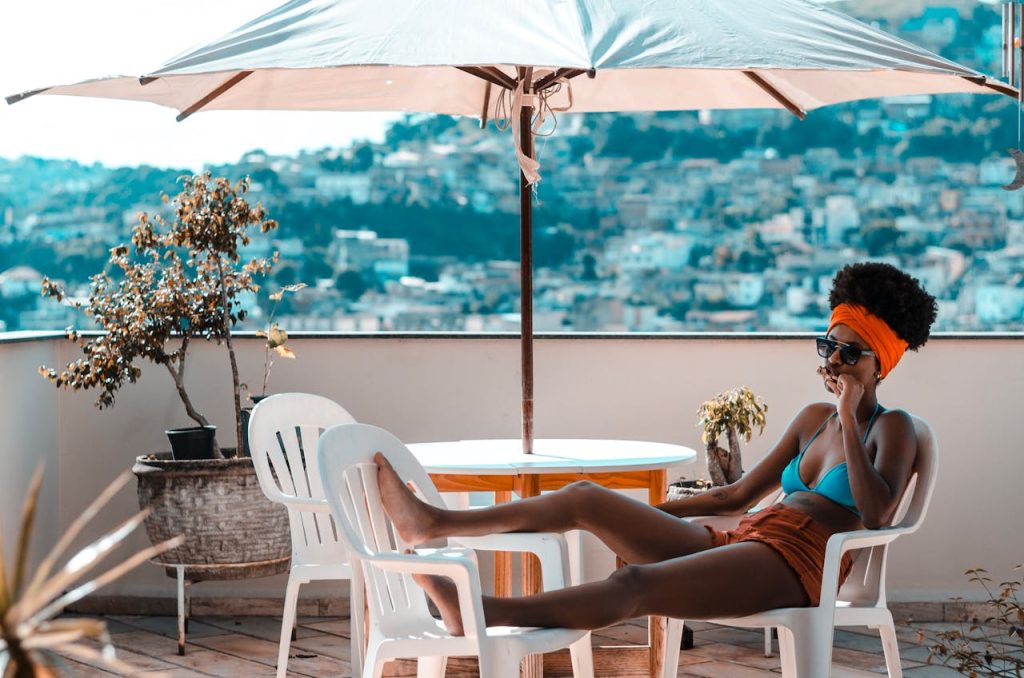 A woman enjoys leisure time on a terrace, lounging beneath a parasol during a sunny day.